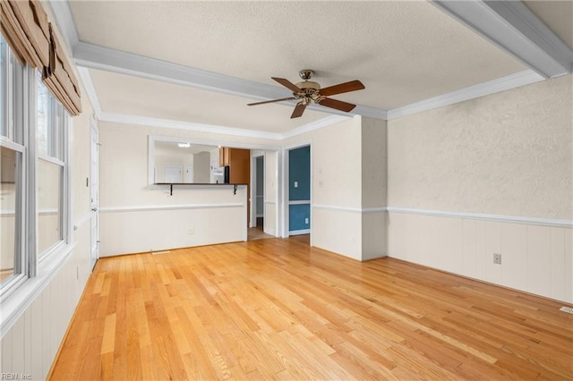 unfurnished room featuring a wainscoted wall, ceiling fan, ornamental molding, a textured ceiling, and light wood-style floors