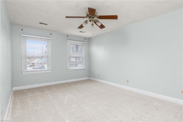 spare room with ceiling fan, visible vents, baseboards, and light colored carpet