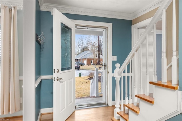 entryway featuring baseboards, ornamental molding, stairway, and light wood-style floors