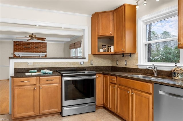 kitchen with stainless steel appliances, decorative backsplash, brown cabinetry, a sink, and dark stone counters