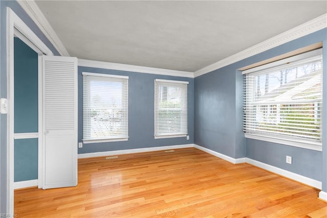 empty room with light wood-type flooring, baseboards, and ornamental molding