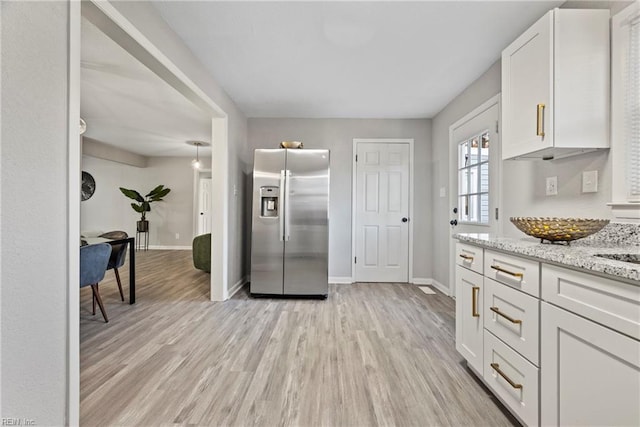 kitchen featuring stainless steel fridge with ice dispenser, light wood-style flooring, white cabinets, light stone countertops, and baseboards