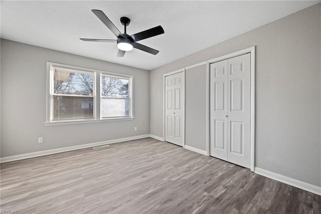 unfurnished bedroom featuring ceiling fan, baseboards, two closets, and wood finished floors