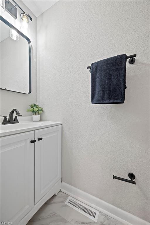 bathroom with baseboards, visible vents, a textured wall, marble finish floor, and vanity