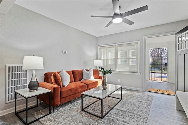 living room with a ceiling fan, visible vents, baseboards, and wood finished floors