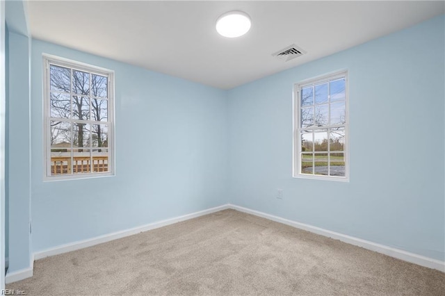 empty room featuring a wealth of natural light, visible vents, light carpet, and baseboards