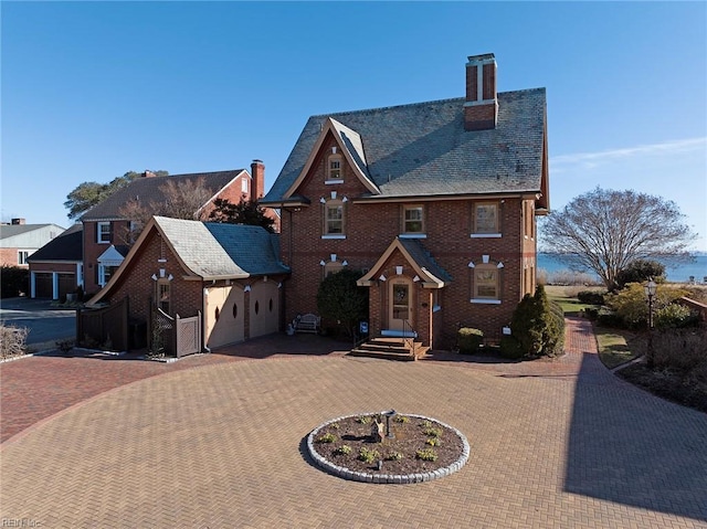 view of front of house with brick siding, curved driveway, a chimney, and a high end roof