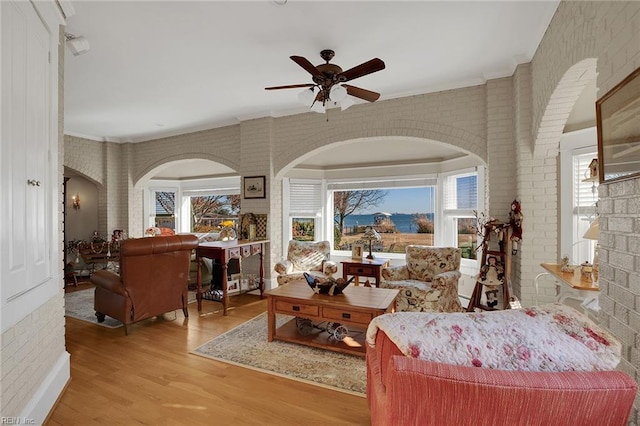 living area with a ceiling fan, ornamental molding, light wood-style flooring, and brick wall