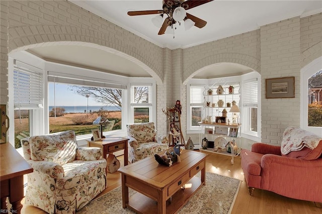 living area featuring light wood-style floors, brick wall, ornamental molding, and a ceiling fan