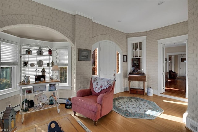 living room with brick wall, crown molding, and light wood finished floors