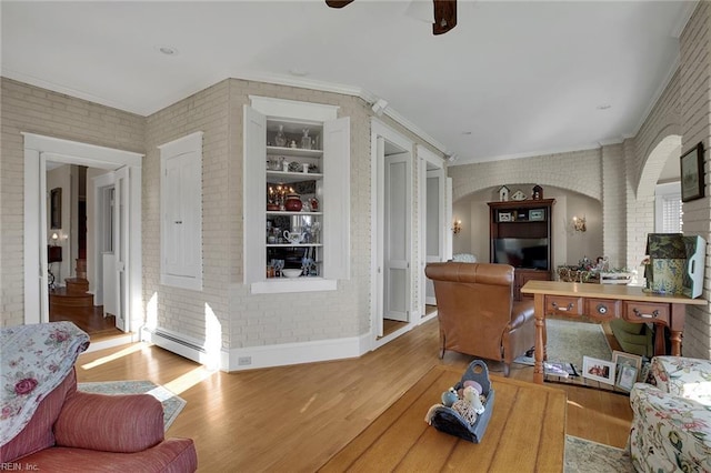 living area with brick wall, crown molding, baseboard heating, and wood finished floors