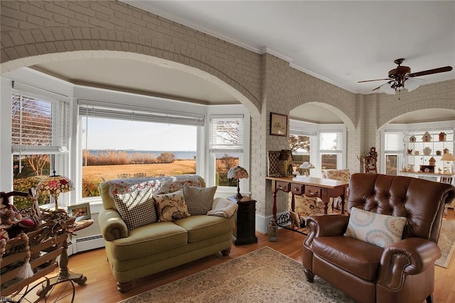 sitting room with light wood-style floors, ornamental molding, brick wall, and a ceiling fan