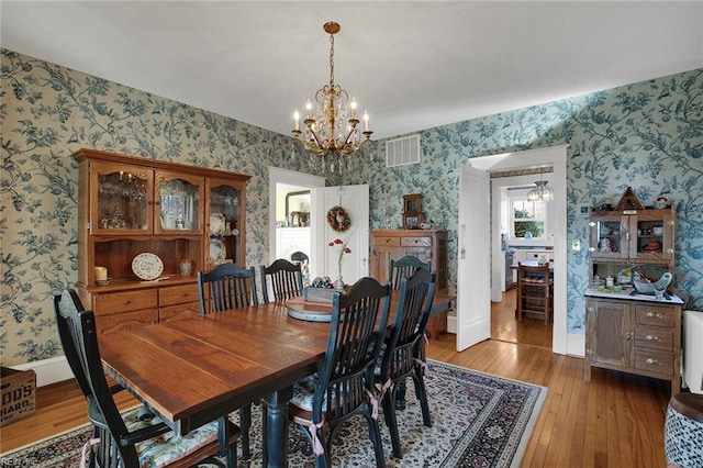 dining space featuring light wood-style floors, a chandelier, visible vents, and wallpapered walls