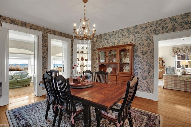 dining room with baseboards, light wood-type flooring, an inviting chandelier, and wallpapered walls