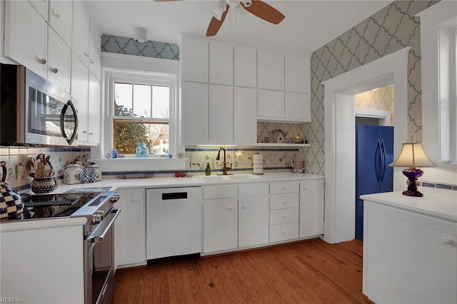 kitchen with a sink, white cabinets, light countertops, appliances with stainless steel finishes, and wallpapered walls