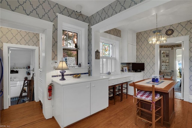 kitchen featuring wood finished floors, white cabinets, light countertops, decorative light fixtures, and wallpapered walls