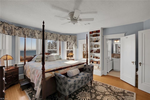 bedroom with a textured ceiling, light wood finished floors, multiple windows, and a water view