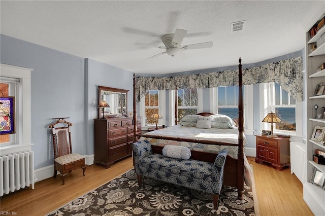 bedroom featuring visible vents, radiator heating unit, a textured ceiling, light wood-type flooring, and baseboards