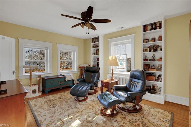 living area featuring radiator, visible vents, ceiling fan, wood finished floors, and baseboards