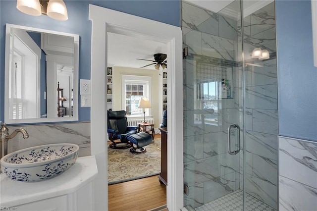 bathroom featuring ceiling fan with notable chandelier, wood finished floors, a stall shower, and a sink