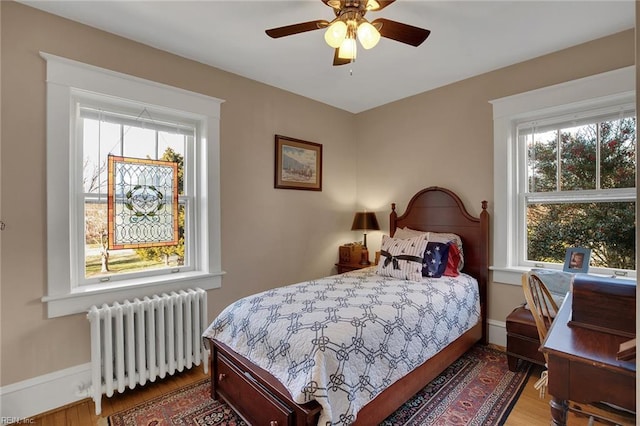 bedroom with baseboards, multiple windows, radiator heating unit, and wood finished floors