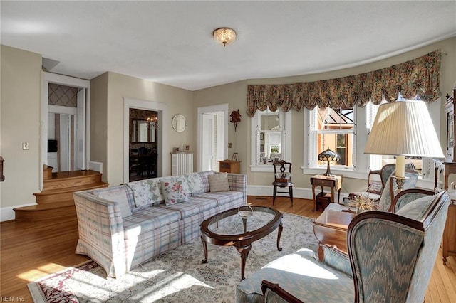 living area featuring light wood-style floors, baseboards, and stairs