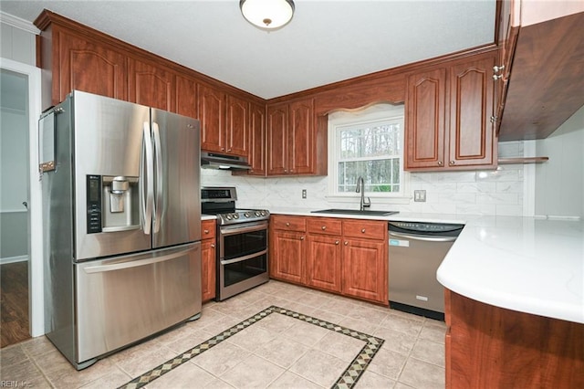 kitchen with appliances with stainless steel finishes, a sink, light countertops, under cabinet range hood, and backsplash