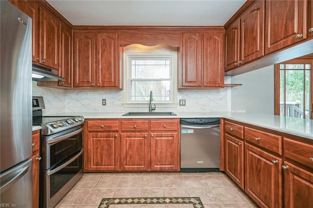 kitchen with under cabinet range hood, a peninsula, a sink, light countertops, and appliances with stainless steel finishes