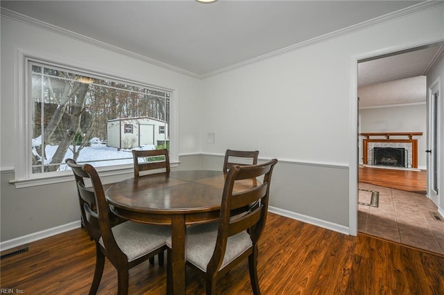 dining space with dark wood-style floors, a fireplace with flush hearth, visible vents, and crown molding