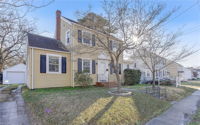 view of front of house with an outdoor structure, a detached garage, roof with shingles, a chimney, and a front yard