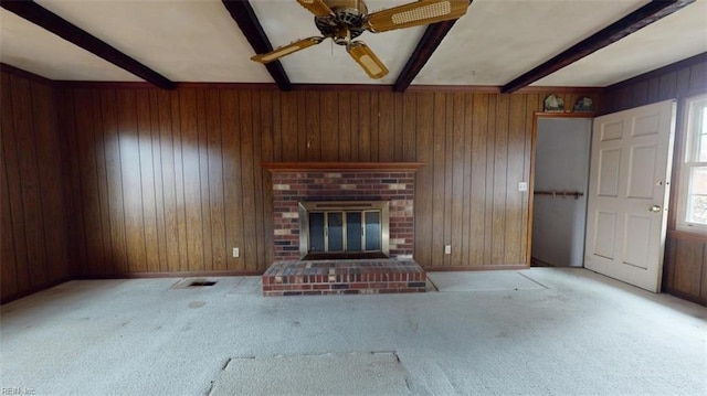 unfurnished living room with light carpet, wood walls, visible vents, a brick fireplace, and beamed ceiling