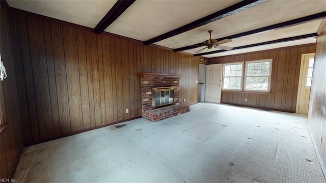 unfurnished living room with wooden walls, light carpet, a fireplace, visible vents, and beam ceiling