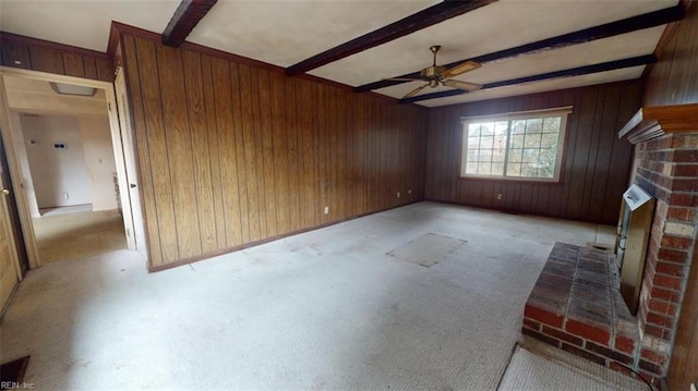 unfurnished living room with a brick fireplace, ceiling fan, beamed ceiling, and wood walls