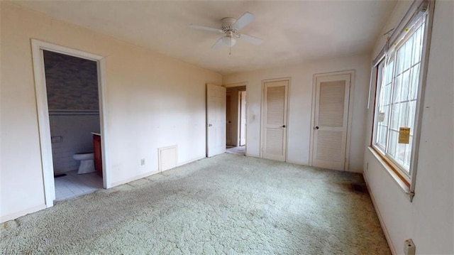 unfurnished bedroom featuring light carpet, two closets, and ensuite bathroom