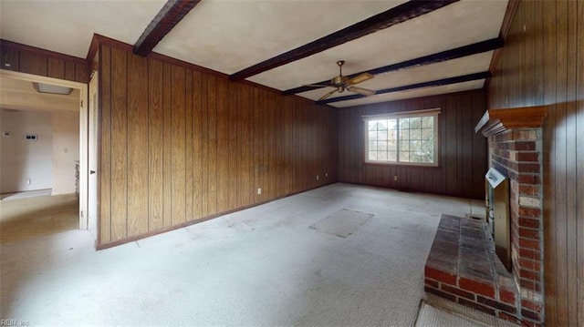 unfurnished living room with beam ceiling, a fireplace, a ceiling fan, light carpet, and wooden walls