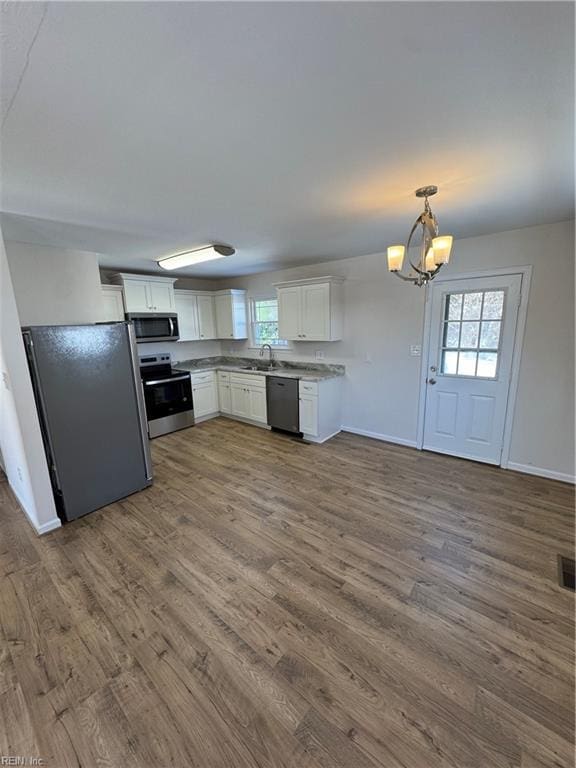 kitchen with dark wood finished floors, stainless steel appliances, hanging light fixtures, white cabinets, and a sink