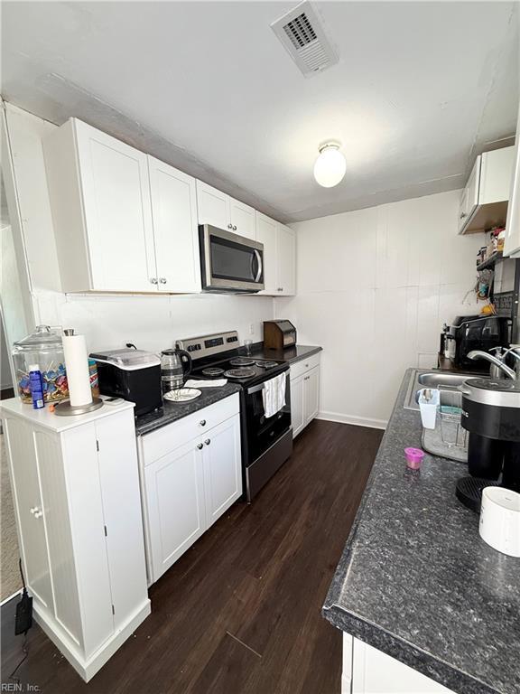 kitchen with visible vents, white cabinets, dark countertops, stainless steel appliances, and a sink