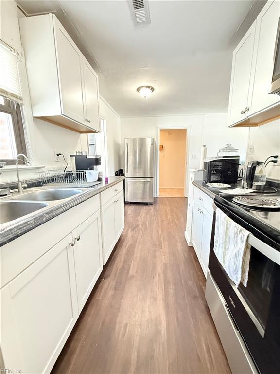 kitchen with dark countertops, appliances with stainless steel finishes, white cabinets, a sink, and wood finished floors