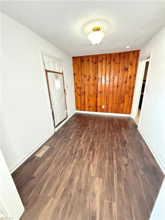 unfurnished room featuring dark wood-style floors, baseboards, visible vents, and wood walls