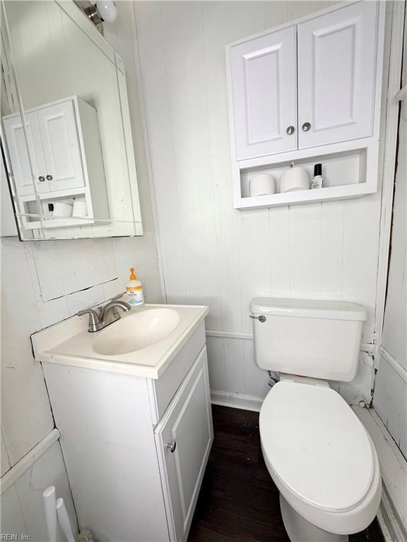 half bathroom featuring toilet, wood finished floors, and vanity