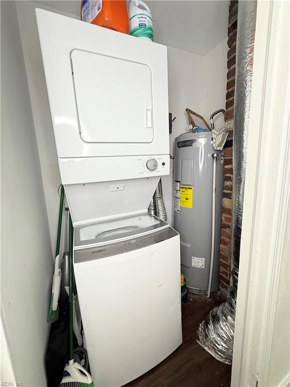 laundry room featuring laundry area, brick wall, dark wood-style flooring, stacked washing maching and dryer, and water heater