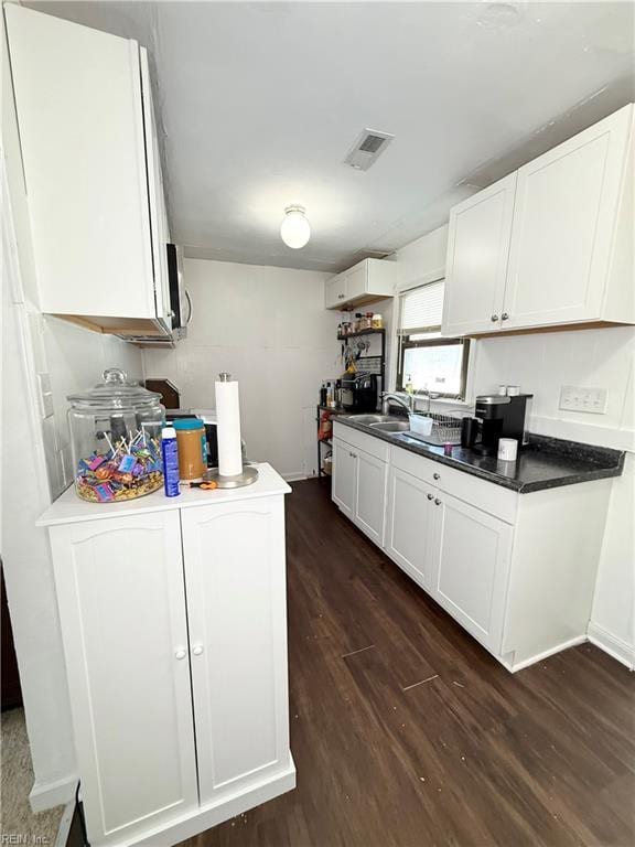 kitchen featuring dark wood finished floors, visible vents, stainless steel microwave, white cabinetry, and a sink