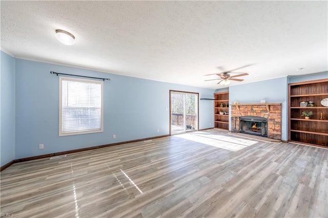 unfurnished living room featuring baseboards, ceiling fan, wood finished floors, a textured ceiling, and a stone fireplace