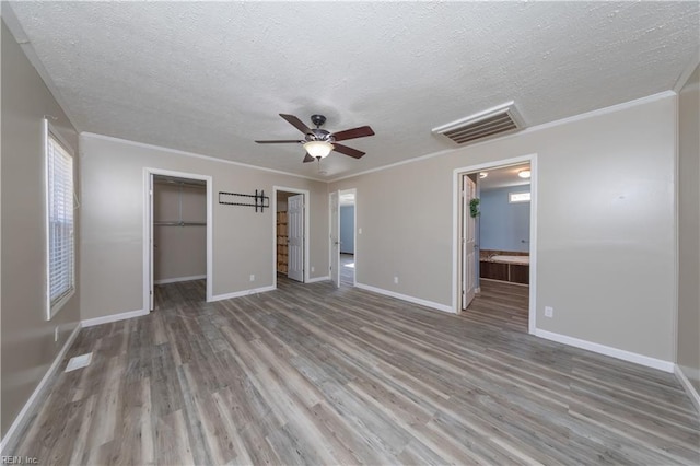 unfurnished bedroom featuring wood finished floors, visible vents, baseboards, ornamental molding, and a walk in closet