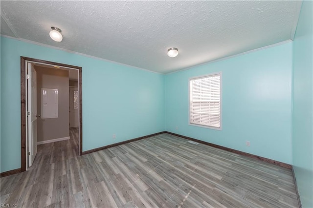 spare room featuring crown molding, a textured ceiling, baseboards, and wood finished floors