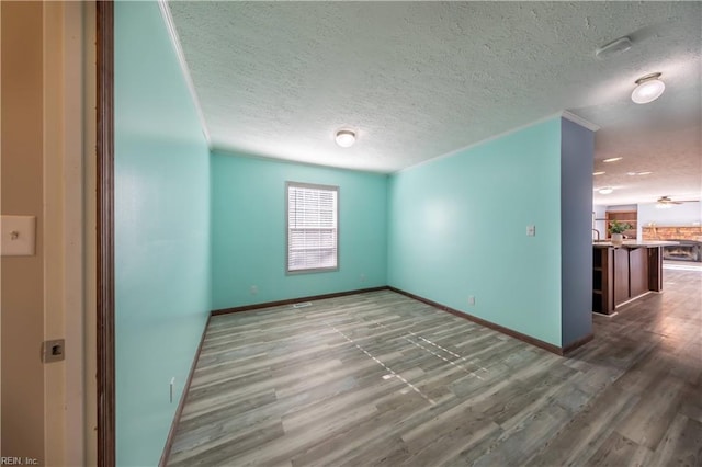 empty room featuring a textured ceiling, ceiling fan, wood finished floors, and baseboards