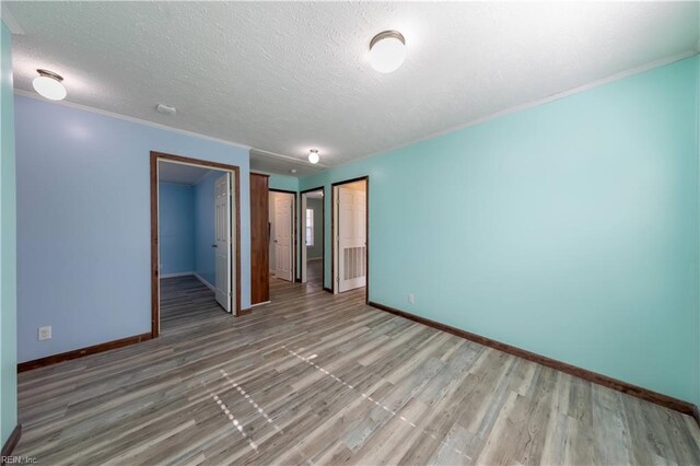 spare room featuring light wood-style floors, baseboards, a textured ceiling, and ornamental molding