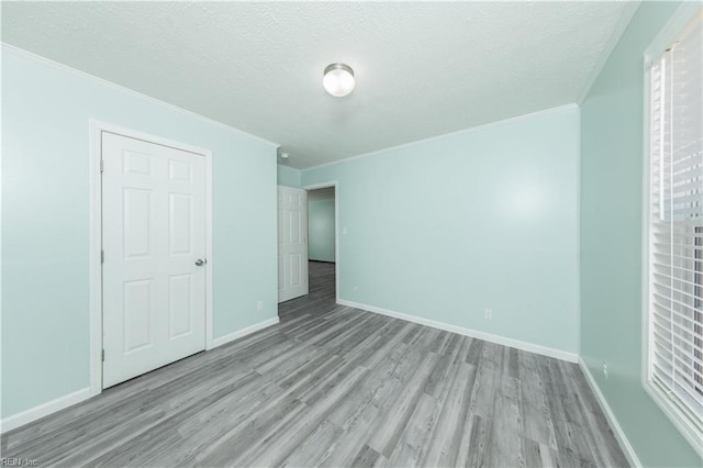 spare room with crown molding, a textured ceiling, baseboards, and wood finished floors