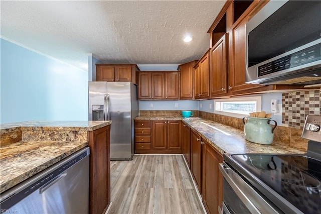 kitchen with a textured ceiling, appliances with stainless steel finishes, brown cabinetry, and light wood-type flooring