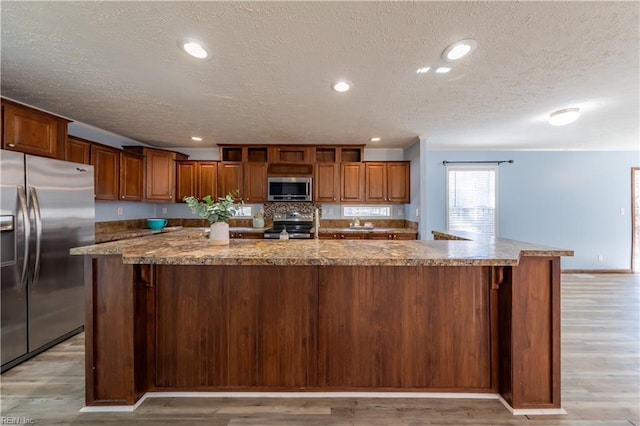 kitchen with stainless steel appliances, recessed lighting, a spacious island, light wood-style flooring, and brown cabinetry